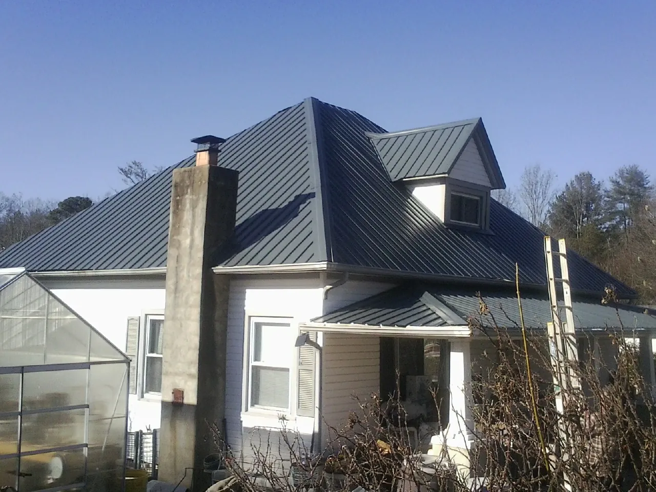 Dark blue standing seam metal roof on a white farmhouse with dormer — Slate & Tile Roof Repair by Roofing Brothers in West Branch