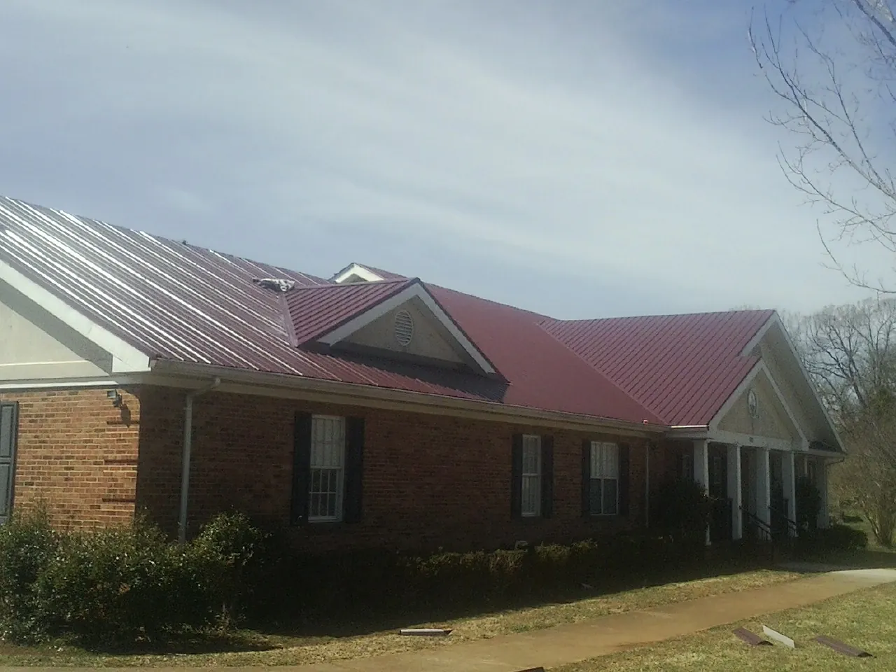 Red metal roof with gabled entries on a long brick building, from a Hail Damage Roof Repair job in West Branch