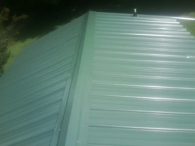New green metal panels meeting at the ridge of a roof — Flat Roof Repair work by our crew in West Branch