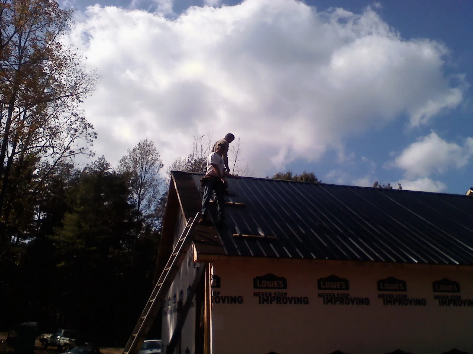 Roofer fastening dark metal panels high against a cloudy sky, from a Roof Inspection job in West Branch