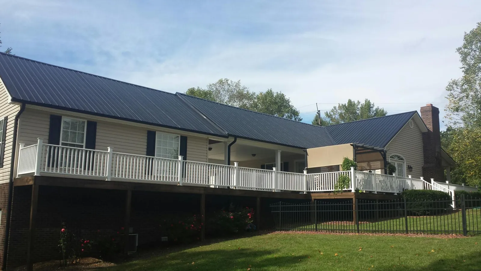 Black metal roof above a long white railed deck on a hillside home in West Branch