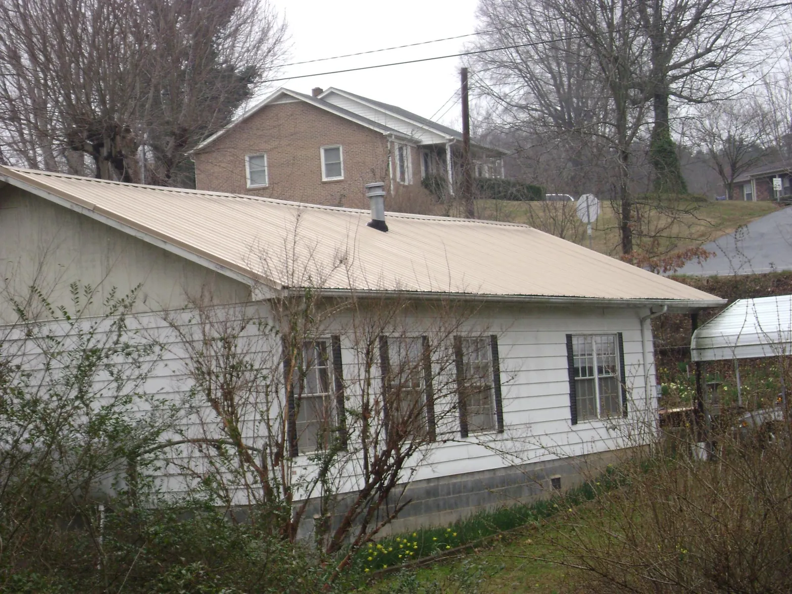 Tan metal roof on a white sided house set into a hillside — Commercial Roofing by Roofing Brothers in West Branch