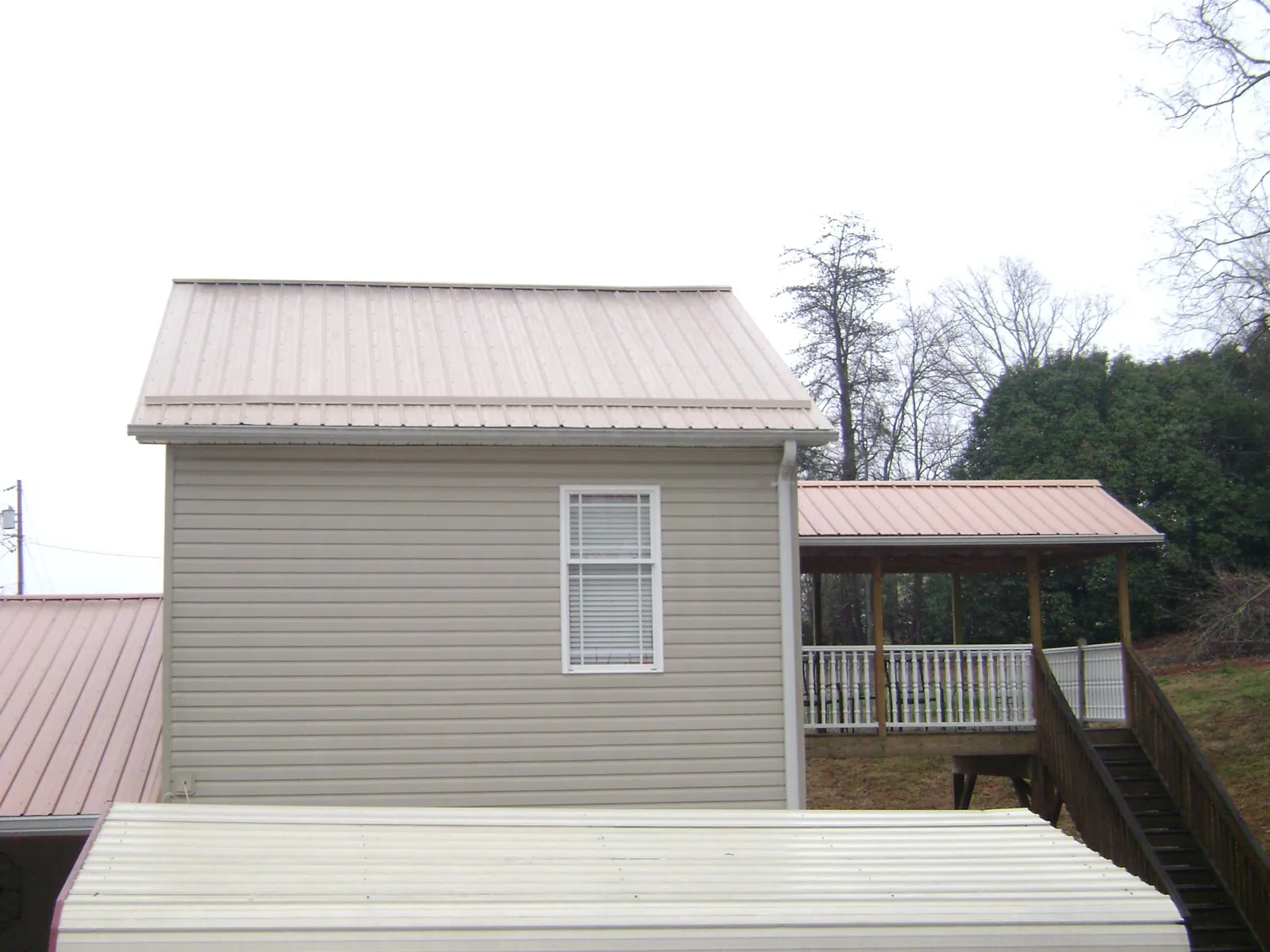 Tan metal roofs on a two story addition and attached porch, from a Roof Replacement job in West Branch