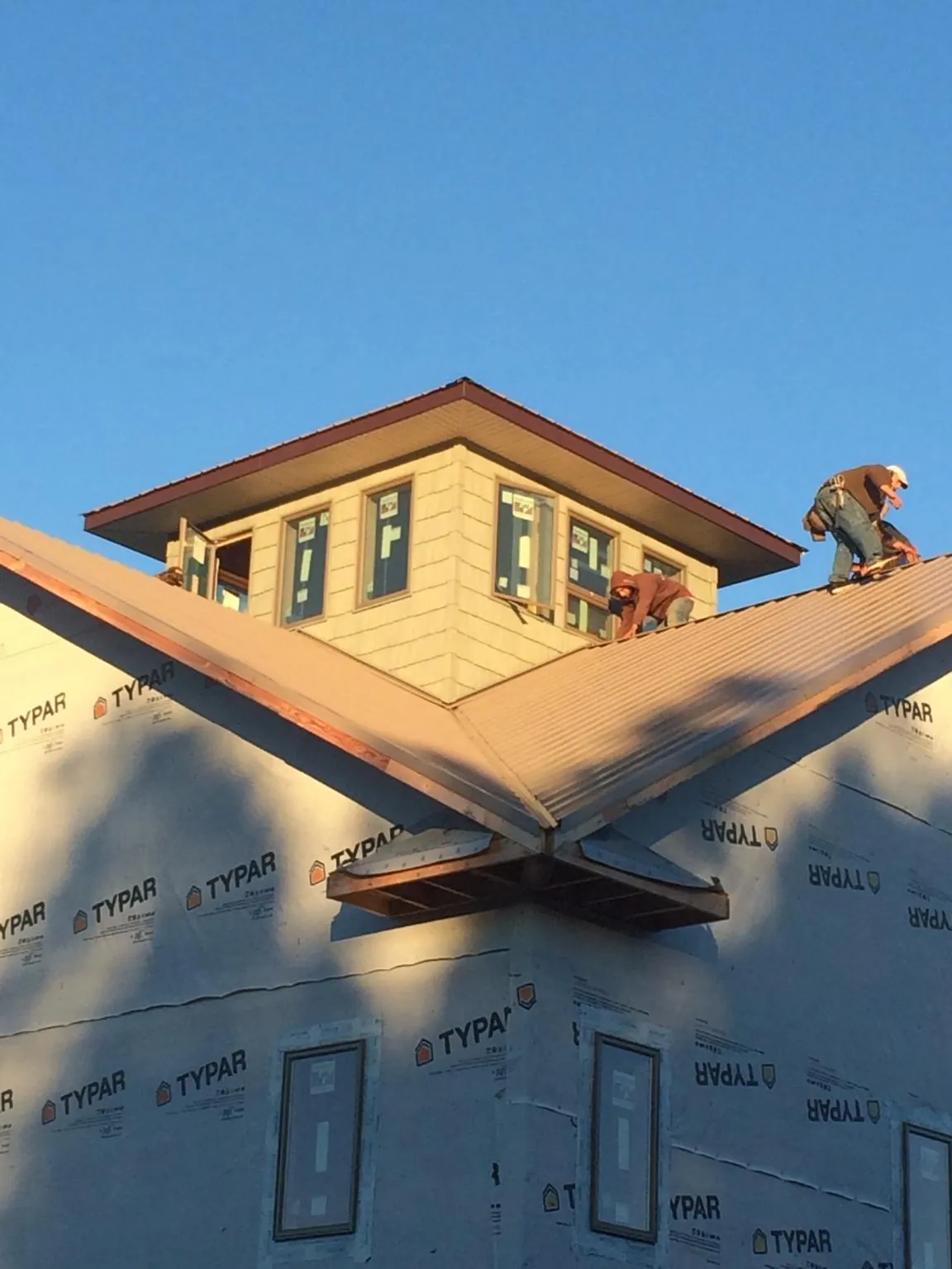 Roofers working around a rooftop cupola on a new metal roof at sunset — Roof Waterproofing in West Branch by Roofing Brothers